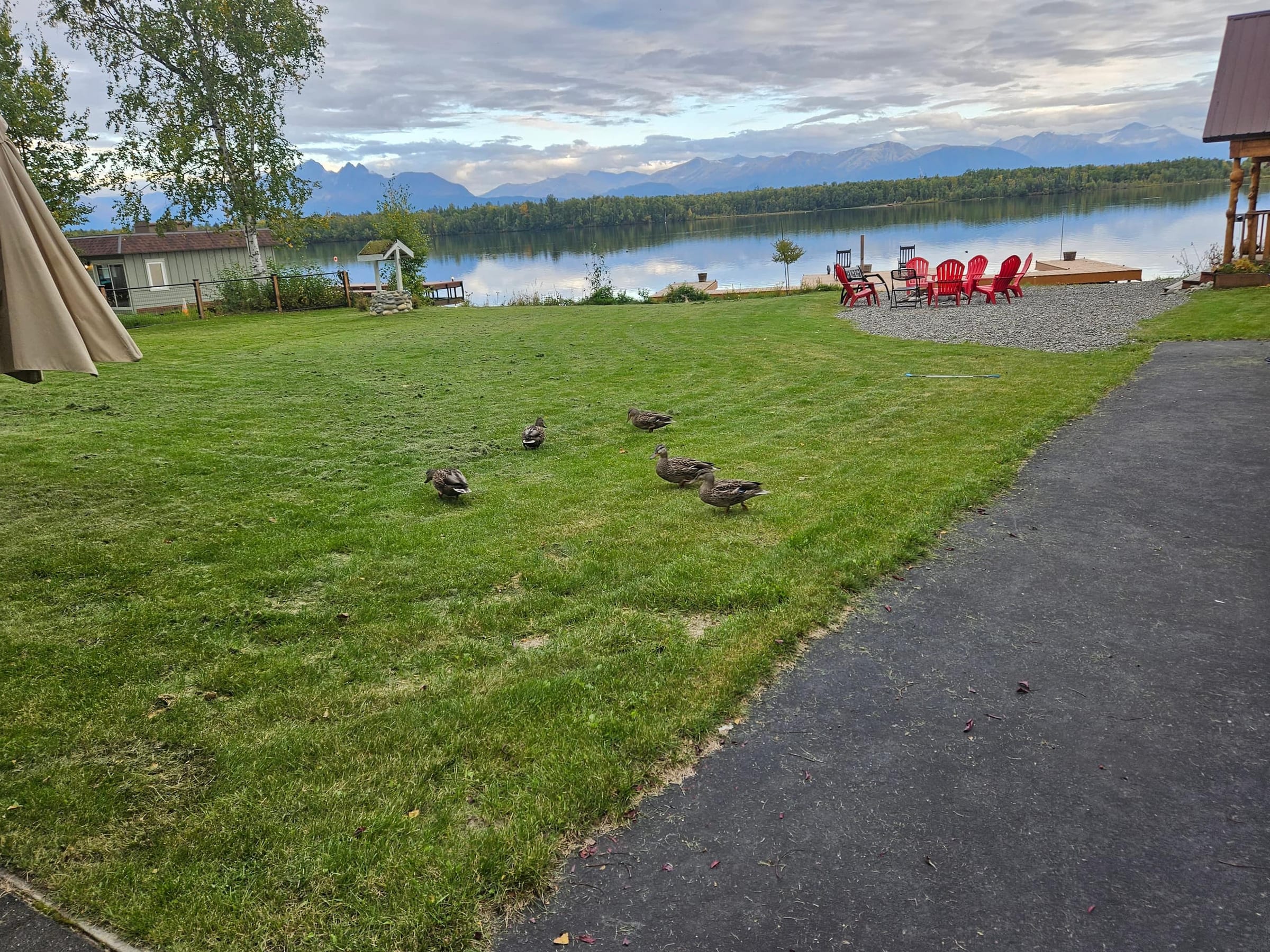 Lawn running down to Lake Lucille, with red Adirondack chairs around the fire pit and mountains across the water