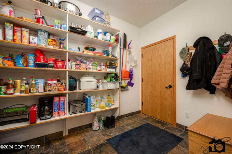 Stocked pantry shelves beside the mudroom coat hooks